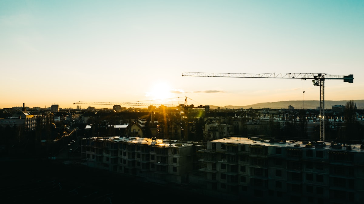 Aerial view of a nonresidential construction site showing crane activity and foundation work.
