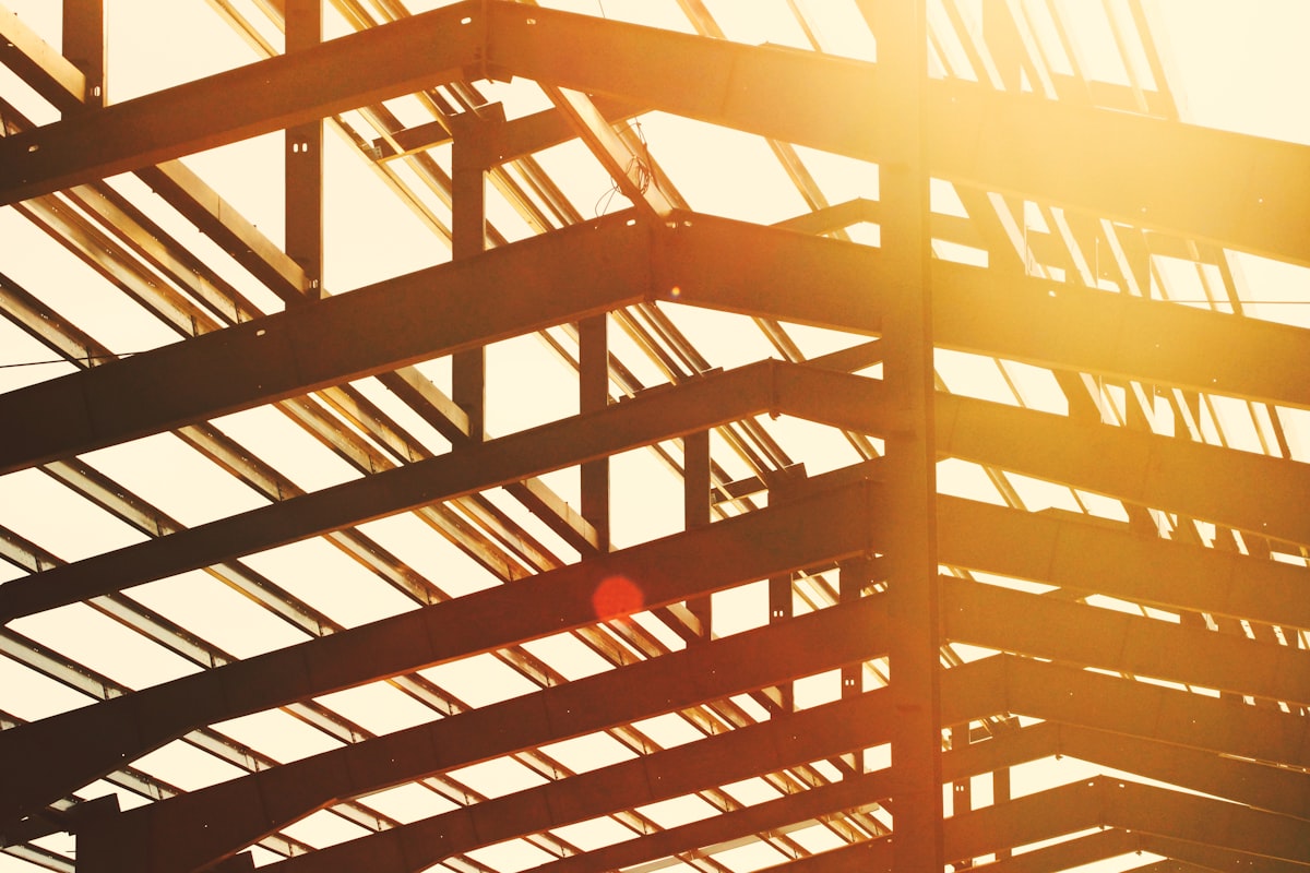 Steel beams stacked in a warehouse, representing surging construction material input costs tracked by GC estimators.