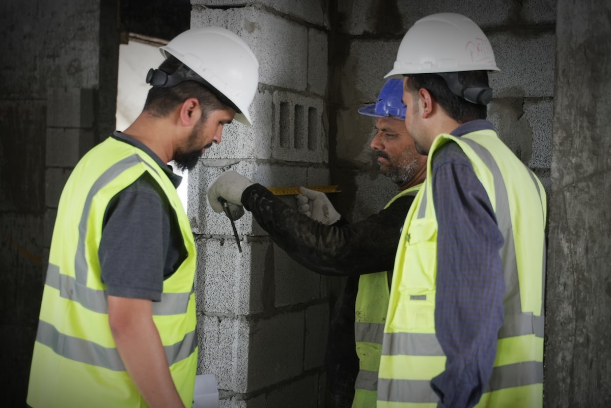 A veteran construction foreman reviewing plans with a younger apprentice on a job site, representing the knowledge transfer challenge facing GC estimating teams.