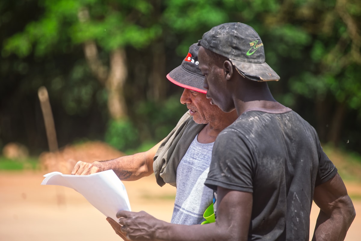 Two general contractors reviewing project documents and discussing subcontractor coordination at a construction site.
